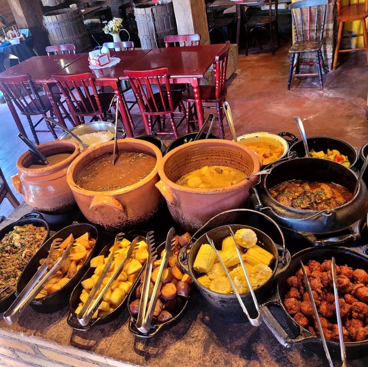 Buffet de comida mineira servido em panelas de barro, com o salão do restaurante ao fundo