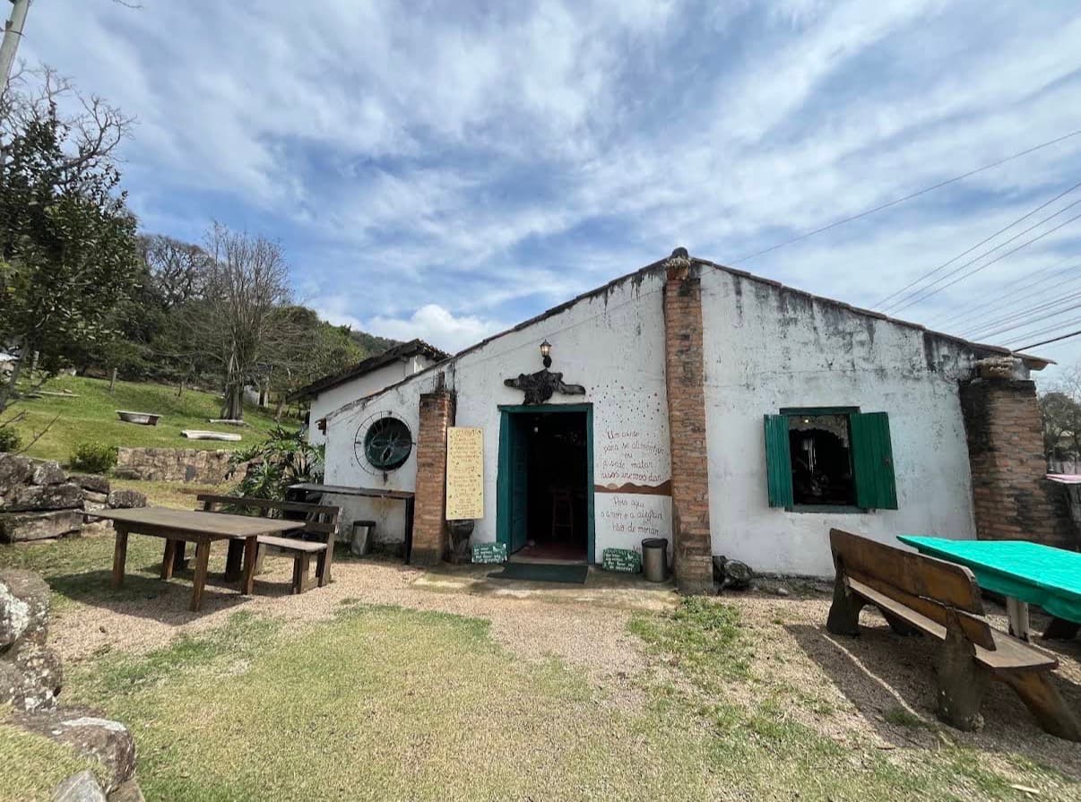 Fachada histórica do Trem de Minas Ribeirão, casarão branco com portas e janelas verdes cercado de natureza