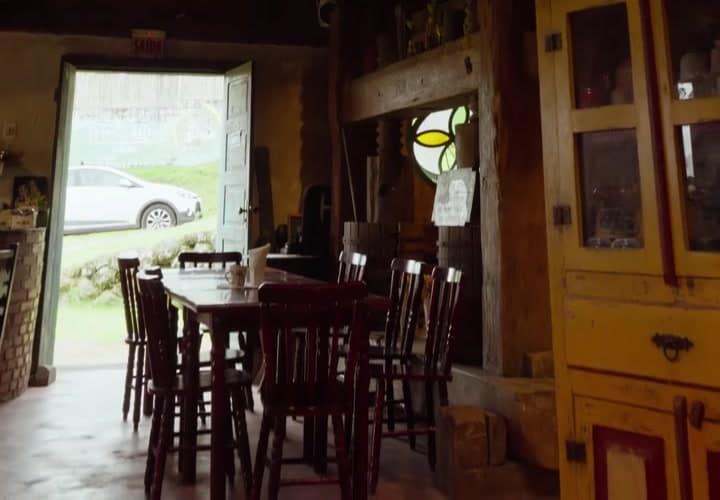 Salão do restaurante com mesas de madeira, porta aberta e armário antigo amarelo